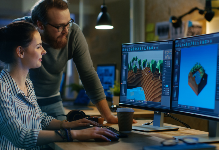 two people look at video screens in a game development lab