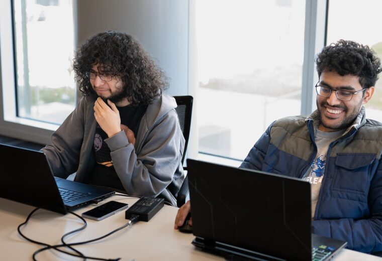 two people sitting abreast look at laptop computers