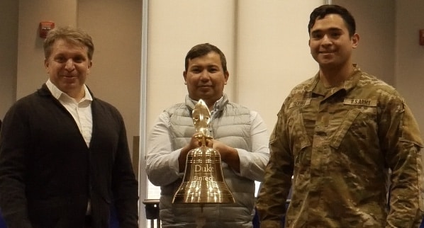 Professor Jake Vestal and students Nurken Abeuov and Mario Trevino ringing the ceremonial bell, marking the start of the trading competition.