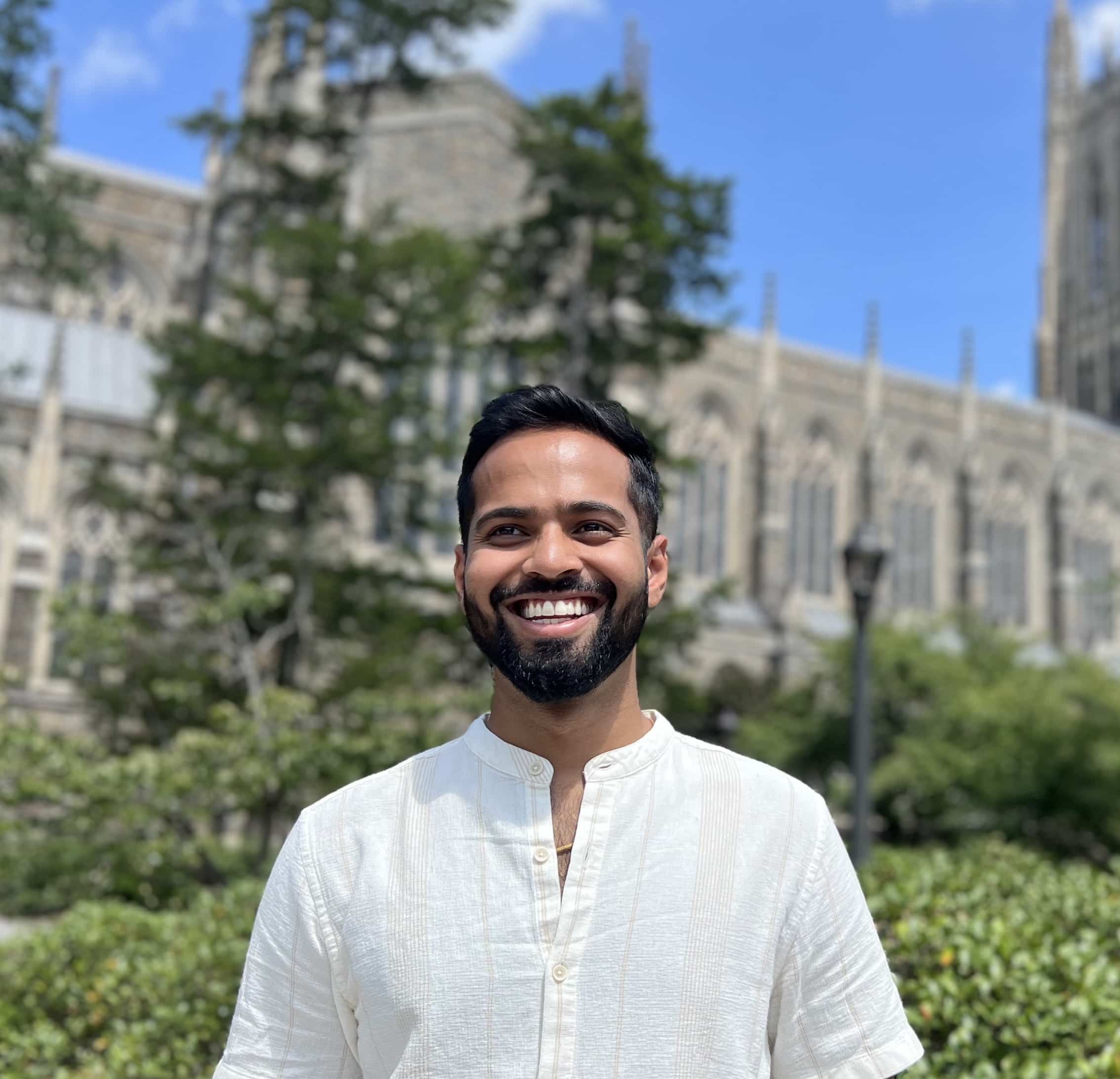 man smiling with trees and buildings behind him