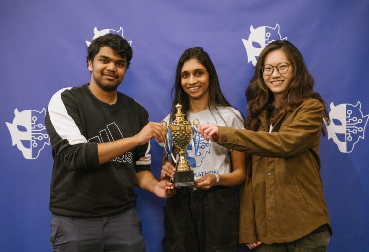 three people hold a gold trophy